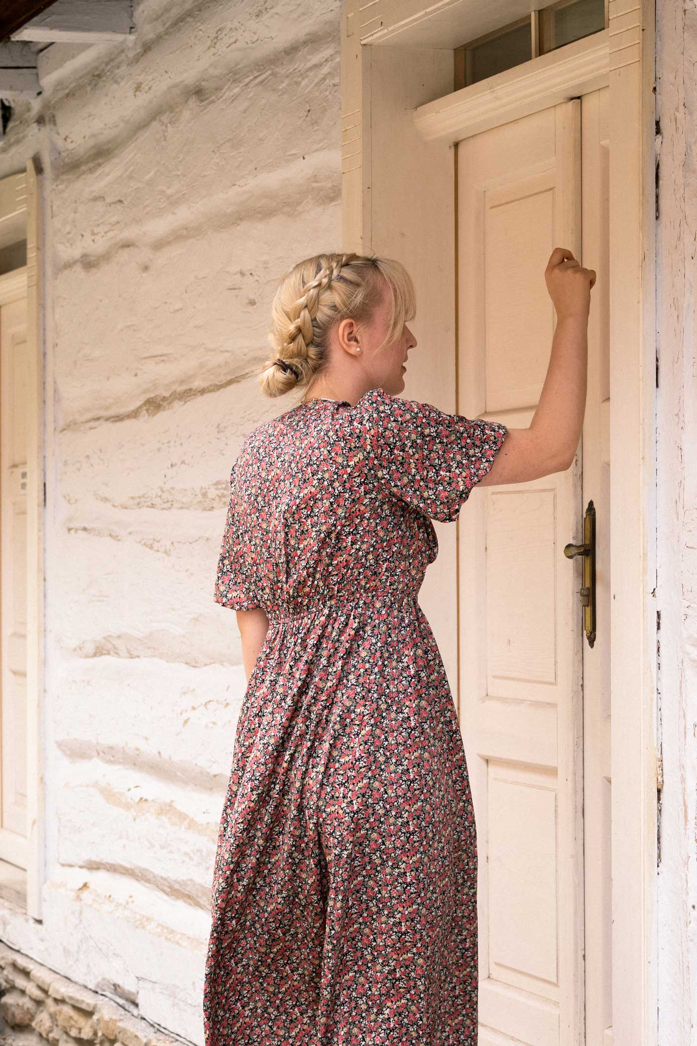 Blond dziewczyna kwiecistej, różowej sukience, puka w białe drzwi białego domu