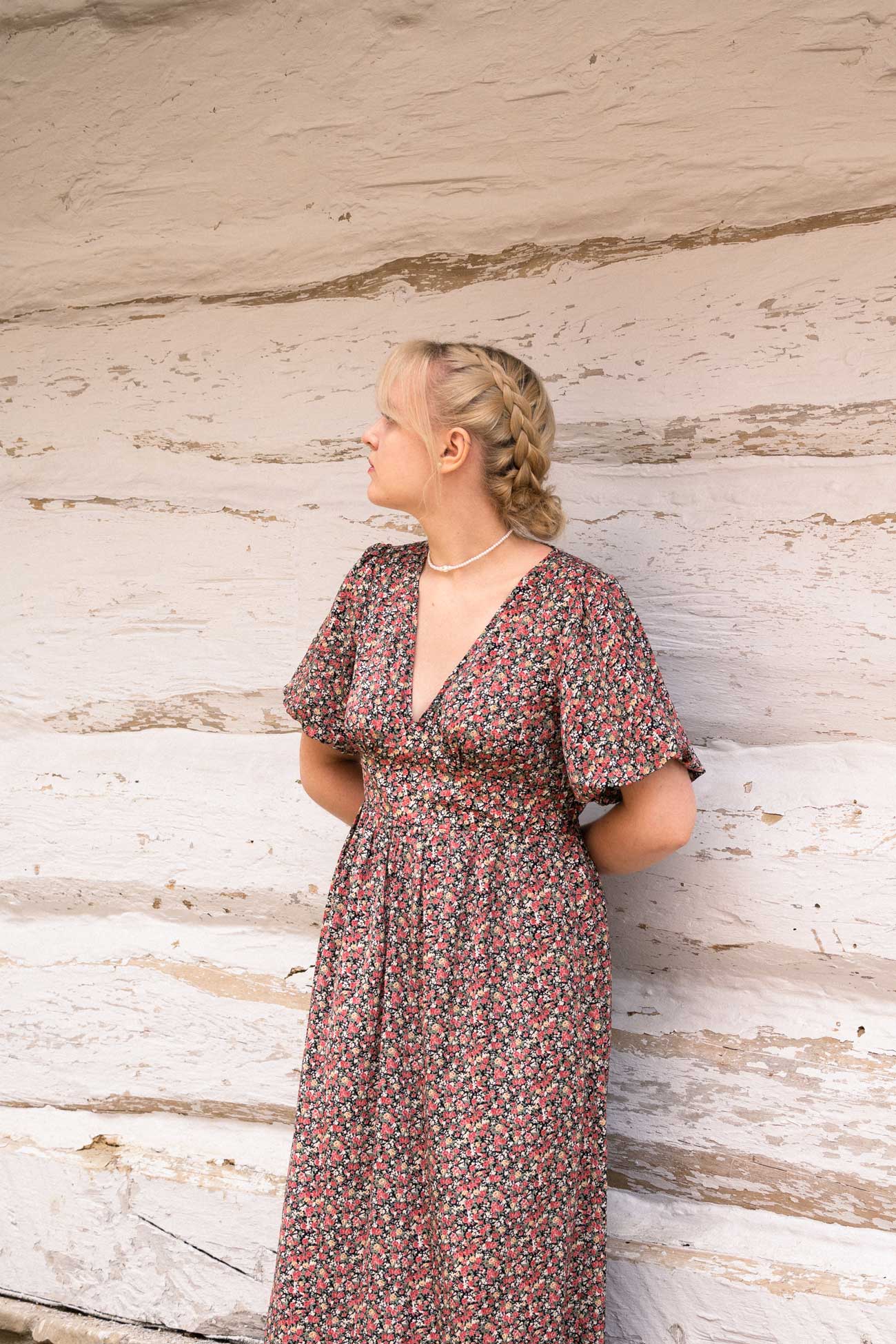 Blond dziewczyna kwiecistej, różowej sukience opiera się o ścianę białego domu