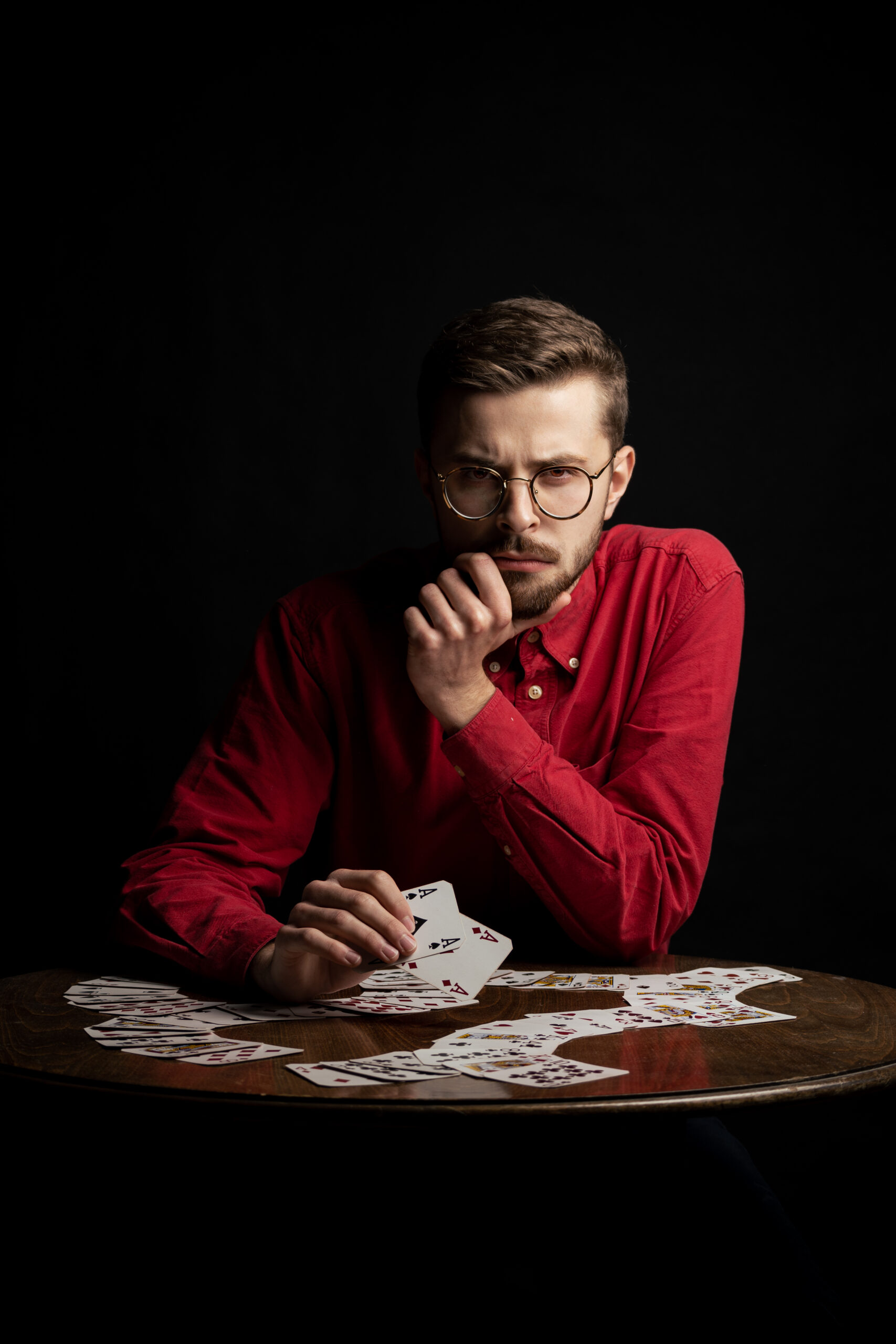Mężczyzna w czerwonej koszuli w okularach gra na stole w karty, które są czerwone