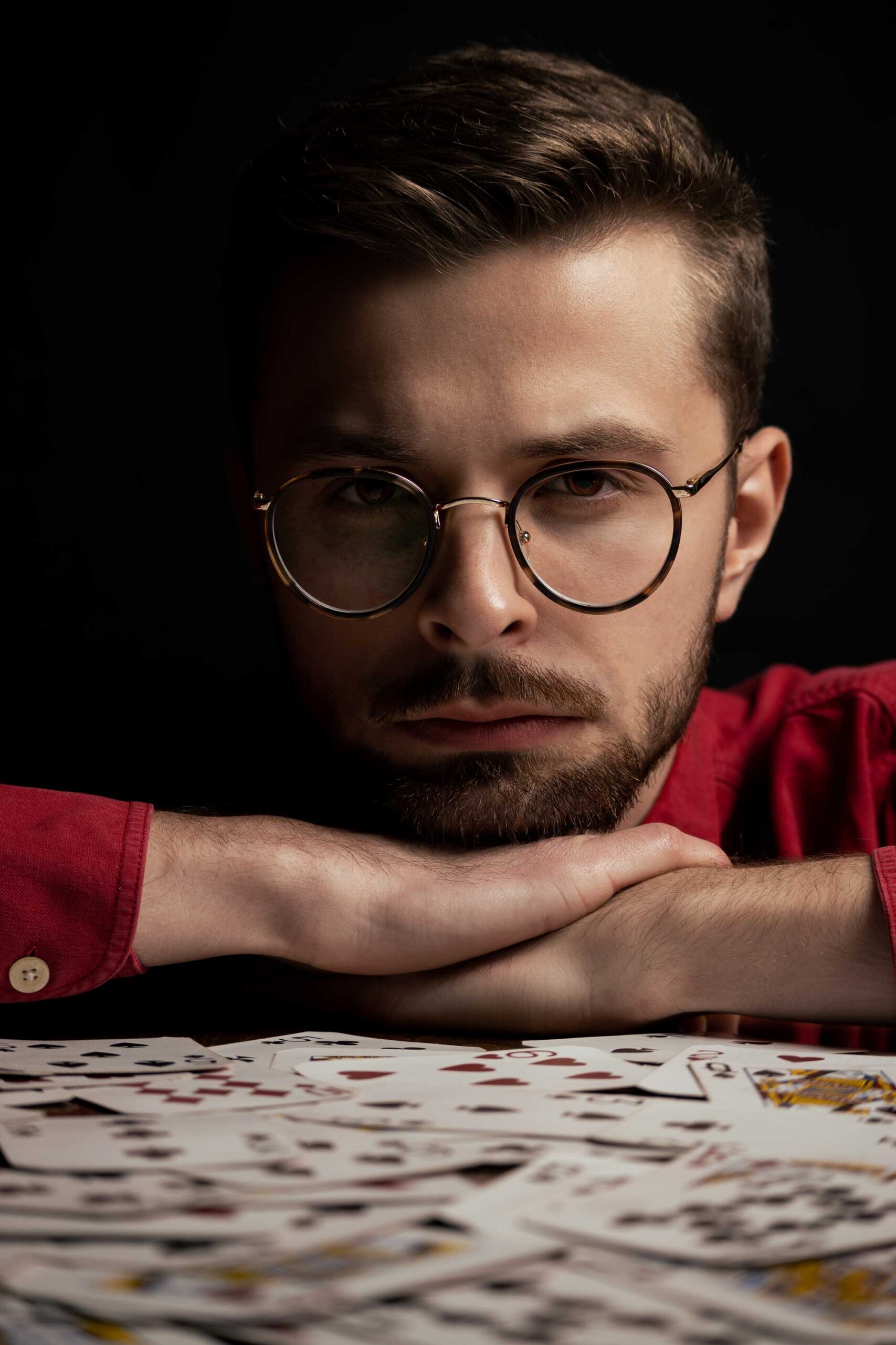 Mężczyzna w czerwonej koszuli w okularach gra na stole w karty, które są czerwone
