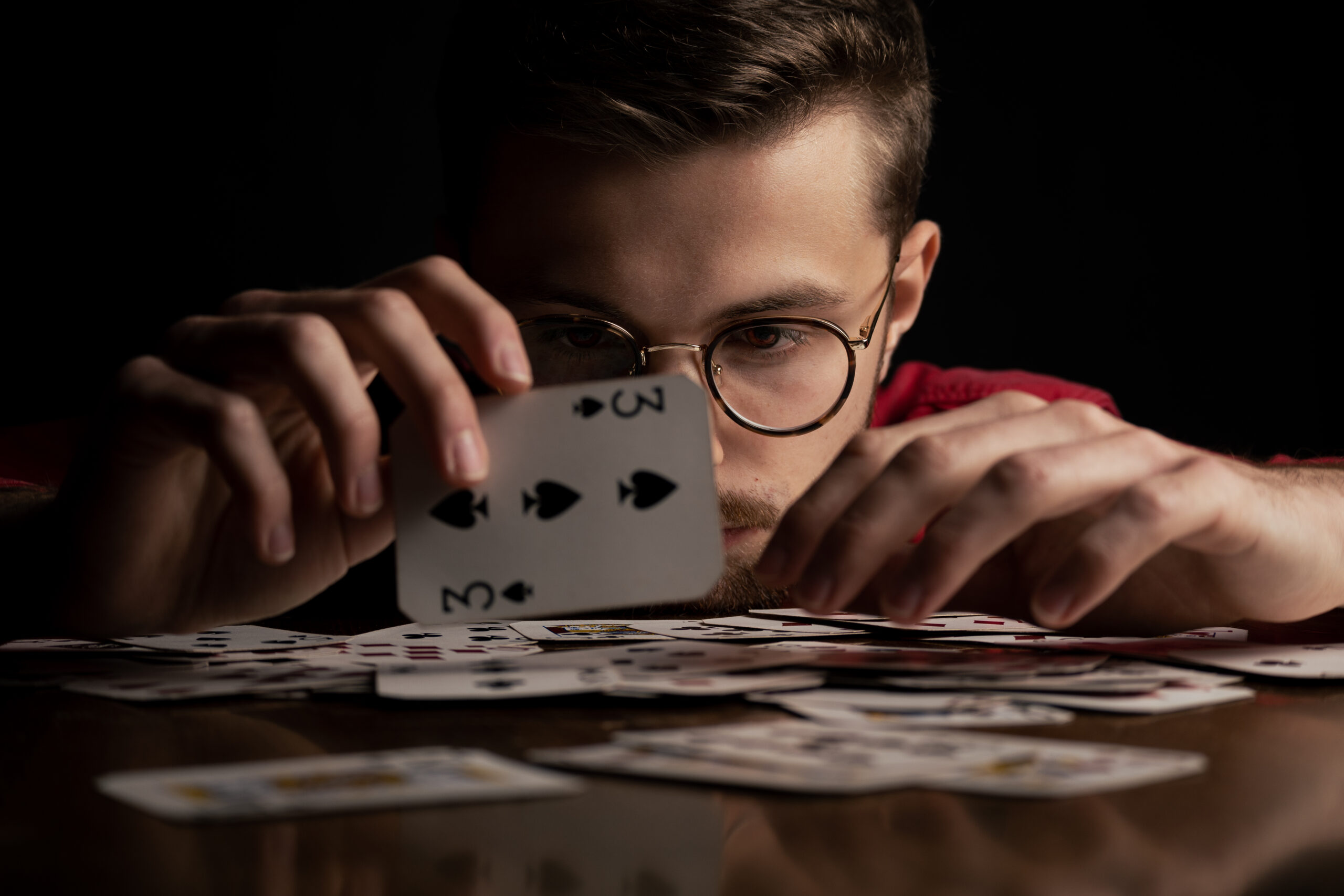 Mężczyzna w czerwonej koszuli w okularach gra na stole w karty, które są czerwone