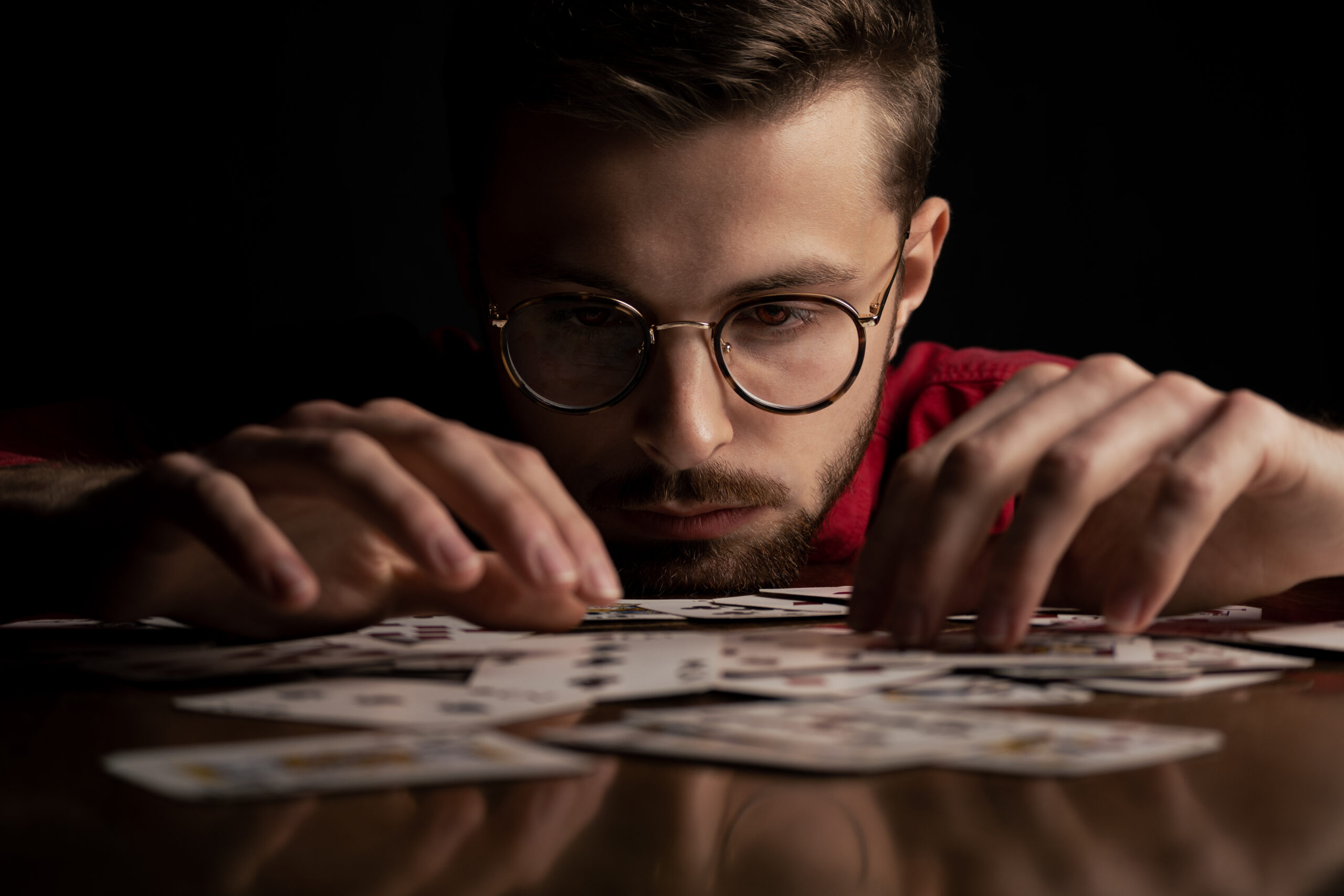 Mężczyzna w czerwonej koszuli w okularach gra na stole w karty, które są czerwone