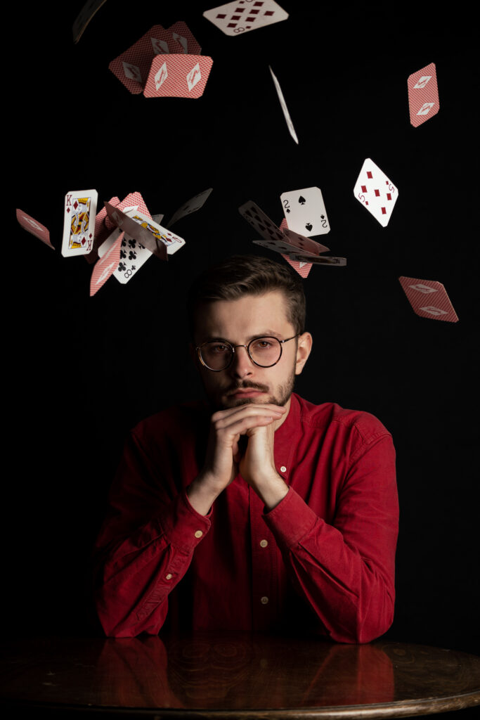Mężczyzna w czerwonej koszuli w okularach gra na stole w karty, które są czerwone. Spadające, latające karty.