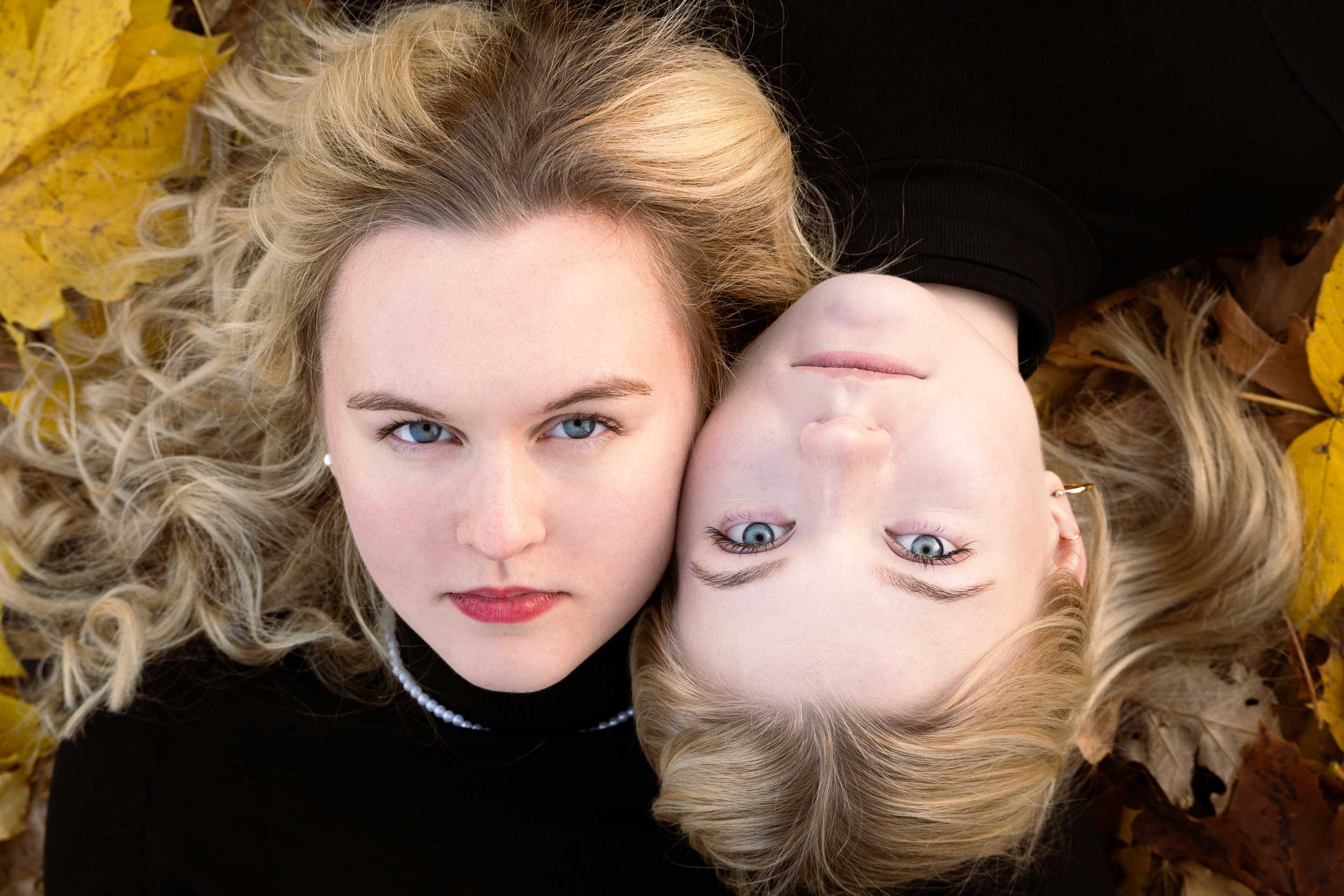 Leżące obok siebie dziewczyny z niebieskimi oczami sykają się policzkami na tle liści