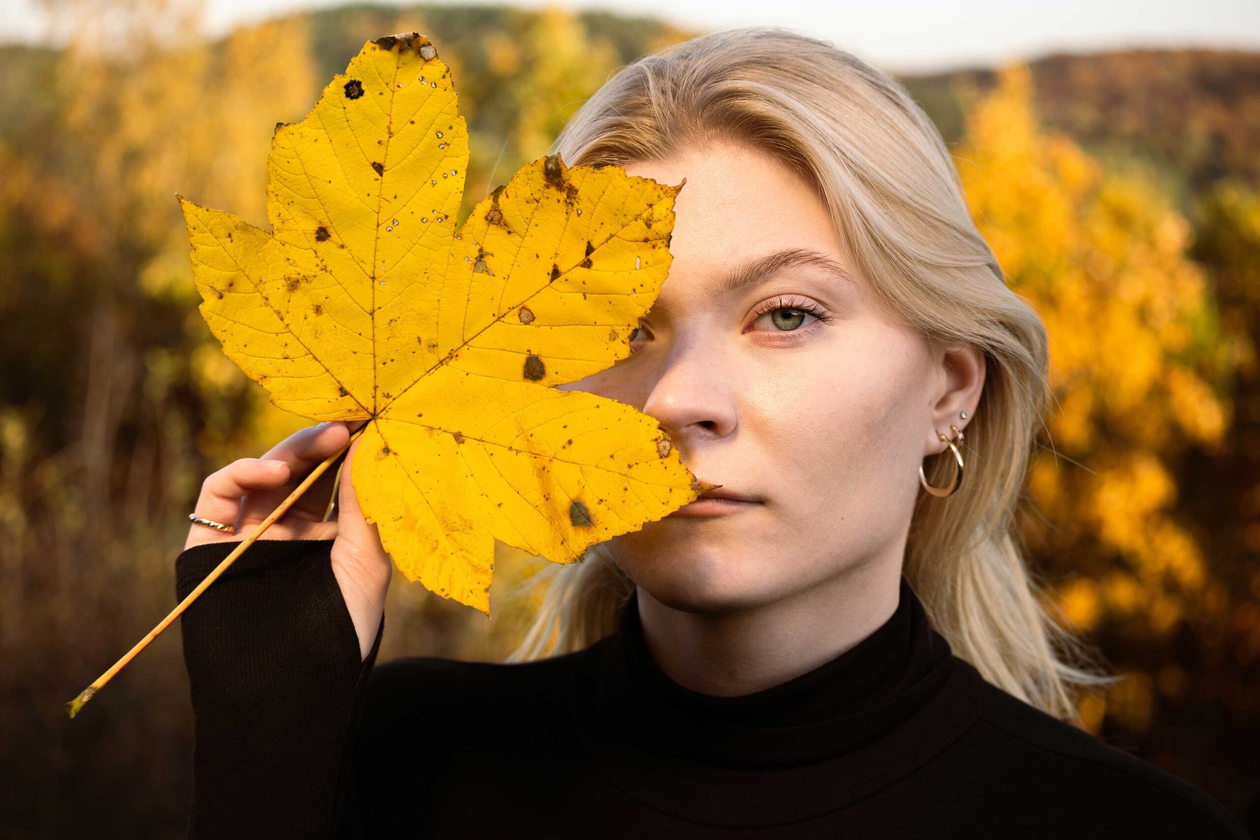 blondynka w jesiennym krajobrazie z liściem w dłoni ubrana w czarny golf