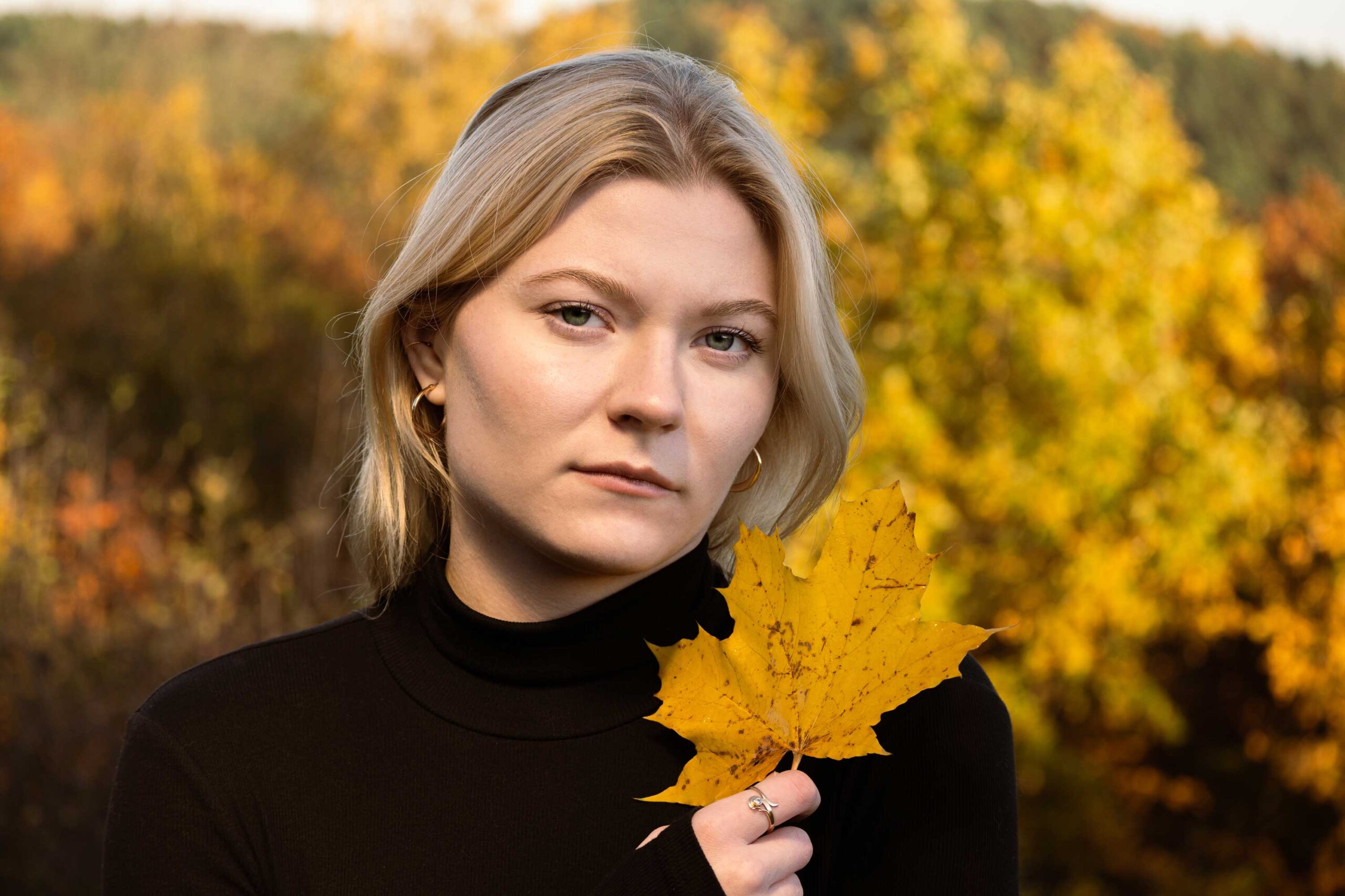 blondynka w jesiennym krajobrazie z liściem w dłoni ubrana w czarny golf