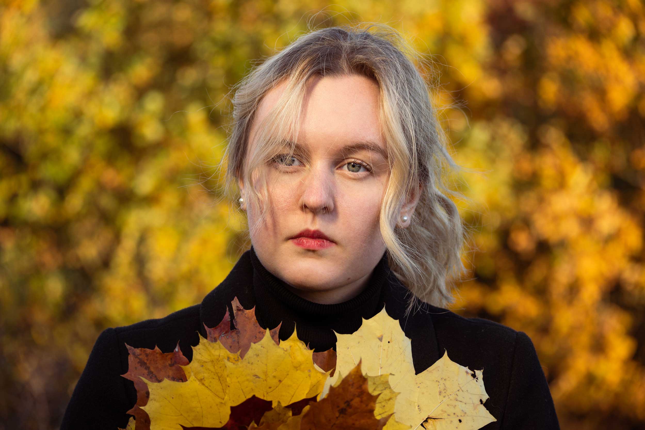 blondynka w jesiennym krajobrazie z liściem w dłoni ubrana w czarny golf