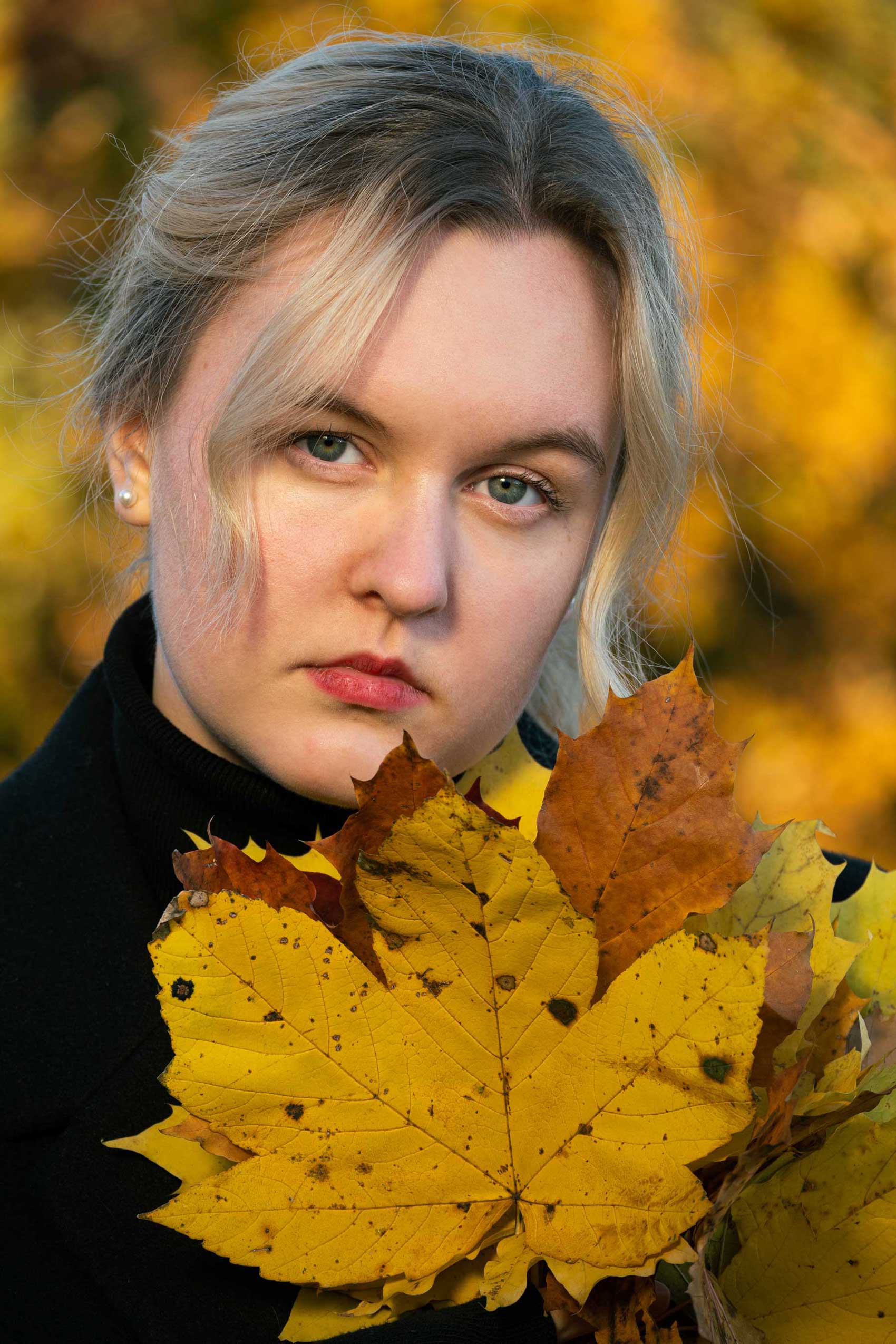 blondynka w jesiennym krajobrazie z liściem w dłoni ubrana w czarny golf