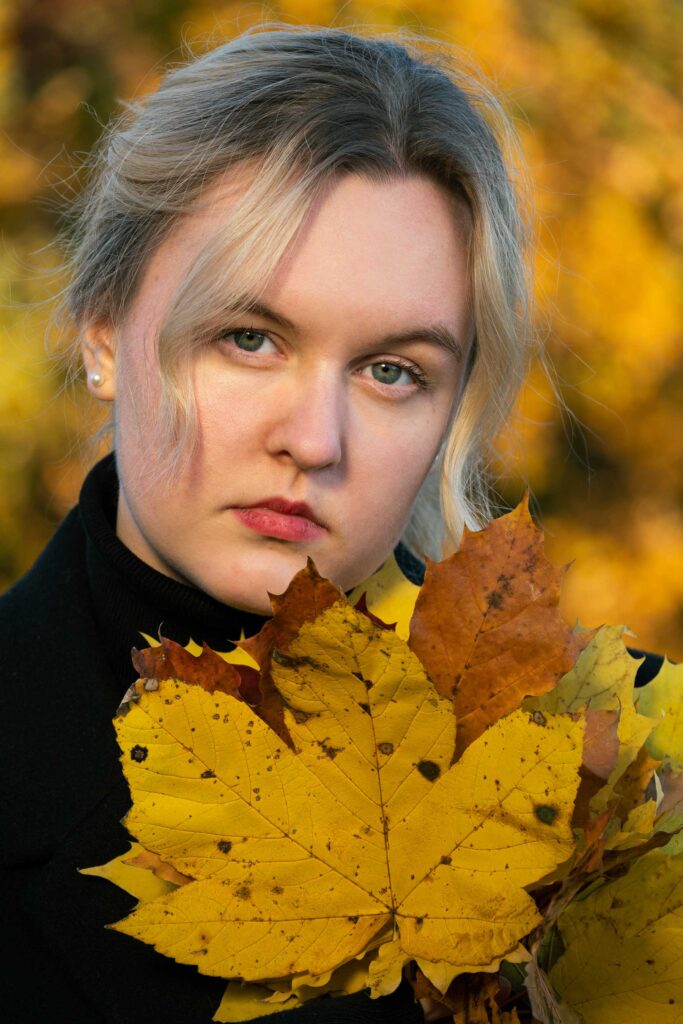 blondynka w jesiennym krajobrazie z liściem w dłoni ubrana w czarny golf