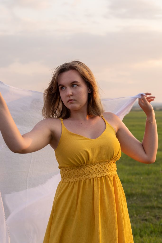 dziewczyna stojąca na łące z białą chustą w dłoniach