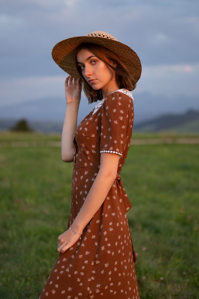 dziewczyna w sukience i kapeluszu stojąca w zachodzie słońca